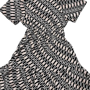 Puede incluir: Vestido estampado en blanco y negro con mangas cortas y cintura fruncida. El vestido presenta un dise&ntilde;o de eslabones de cadena repetidos en blanco y beige sobre un fondo negro. La falda tiene un dobladillo con volantes.