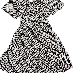 Puede incluir: Vestido estampado en blanco y negro con mangas cortas y falda escalonada. El vestido presenta un dise&ntilde;o repetitivo en forma de cadena blanca sobre un fondo negro. La cintura est&aacute; ce&ntilde;ida con el&aacute;stico y el escote es en V.
