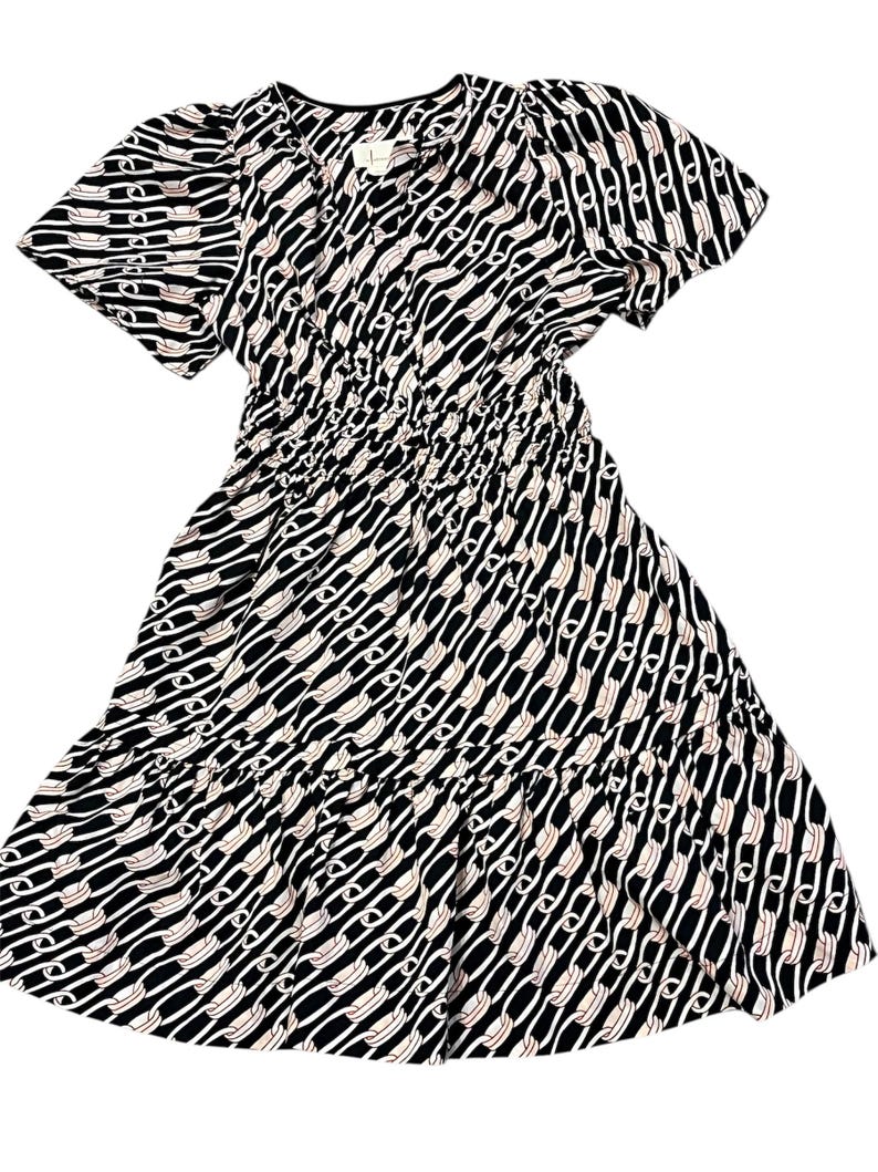 Puede incluir: Vestido estampado en blanco y negro con mangas cortas y falda escalonada. El vestido presenta un dise&ntilde;o repetitivo en forma de cadena blanca sobre un fondo negro. La cintura est&aacute; ce&ntilde;ida con el&aacute;stico y el escote es en V.