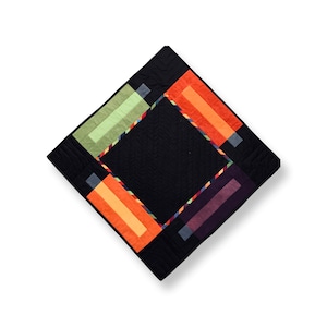 May include: A black square quilt with a colourful geometric design. The quilt features a central black square surrounded by four squares in shades of green, orange, and purple.