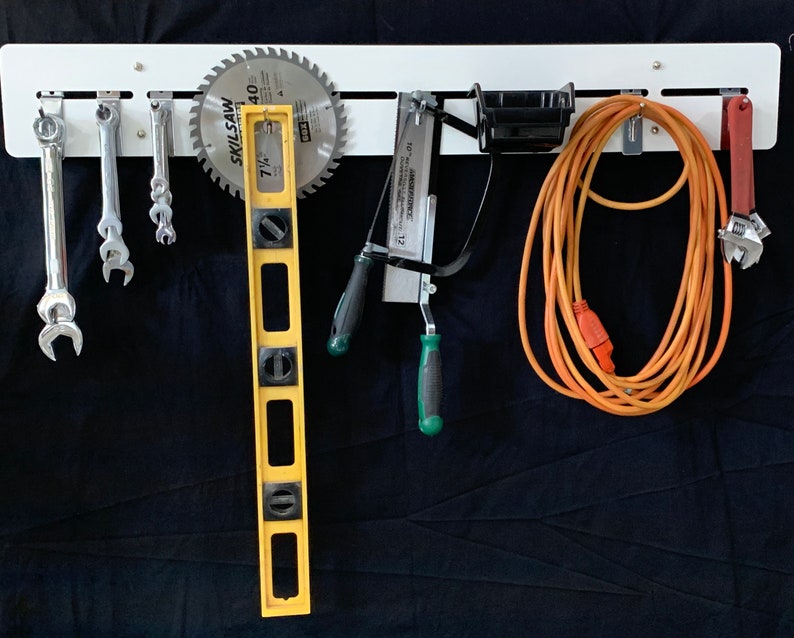 May include: White metal tool organizer with various tools hanging on it, including wrenches, a level, a saw blade, a saw, an extension cord, and a pair of pliers.