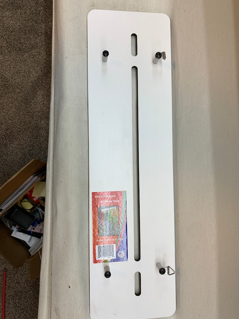 May include: White metal wall mount with four black screws and a label that reads "Rita's Riches, 12-1/2" Door Rack, www.ritariches.com".