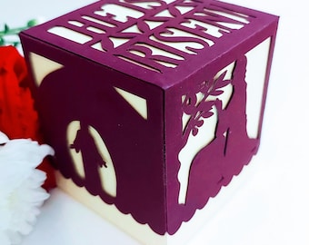 May include: A burgundy papercraft box with a cut-out design of a figure with a cross and the words "He is Risen".