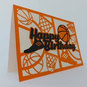 May include: Orange card with a black and white basketball theme. The card says "Happy Birthday" with a basketball, a basketball hoop, and a basketball shoe.