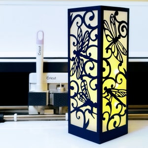 May include: A black and white paper lantern featuring a dragonfly design. The lantern is lit from within, casting a warm glow.