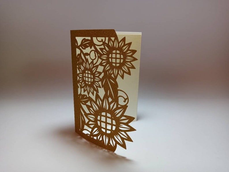 May include: A gold card with a cut-out design of sunflowers and leaves. The card is folded in half and the inside is blank.