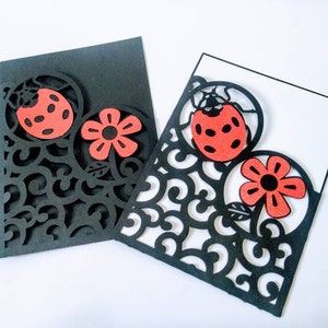 May include: Two black cardstock cards with intricate cut-out designs. The designs feature a red ladybug and a red flower. The cards are perfect for crafting and scrapbooking.