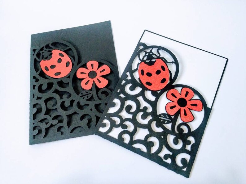 May include: Two black cardstock cards with intricate cut-out designs. The designs feature a red ladybug and a red flower. The cards are perfect for crafting and scrapbooking.