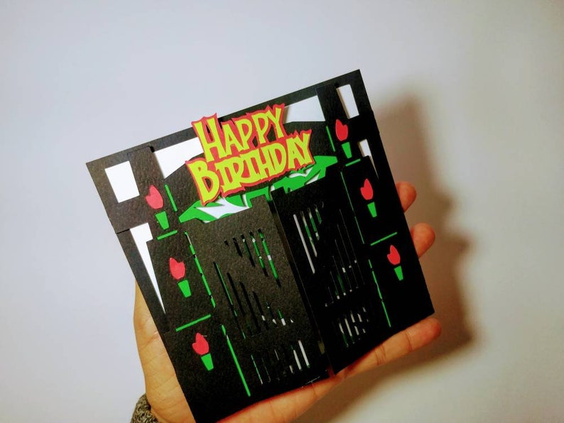 May include: A black and green 3D pop-up card with a gate design. The card has a red and yellow "Happy Birthday" message on the front.
