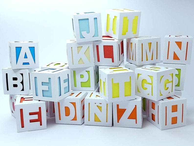 May include: A stack of white cardboard boxes with colourful letters cut out of them. The letters spell out the alphabet.