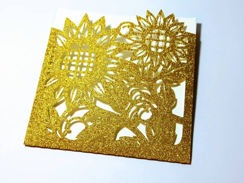 May include: Gold glitter card with a cut-out design of two sunflowers. The card is folded in half and has a white interior.