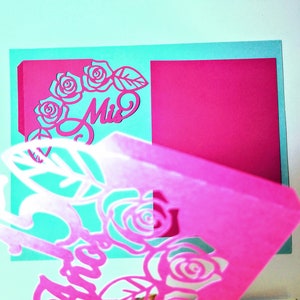 May include: A pink and teal paper craft with a cut-out design of roses and the word "Miss".