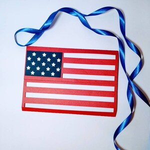 May include: A red, white, and blue paper American flag with a blue ribbon.