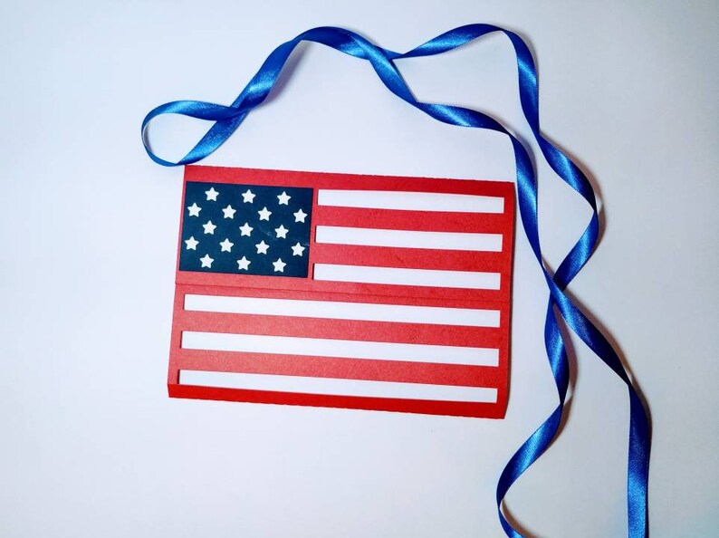 May include: A red, white, and blue paper American flag with a blue ribbon.