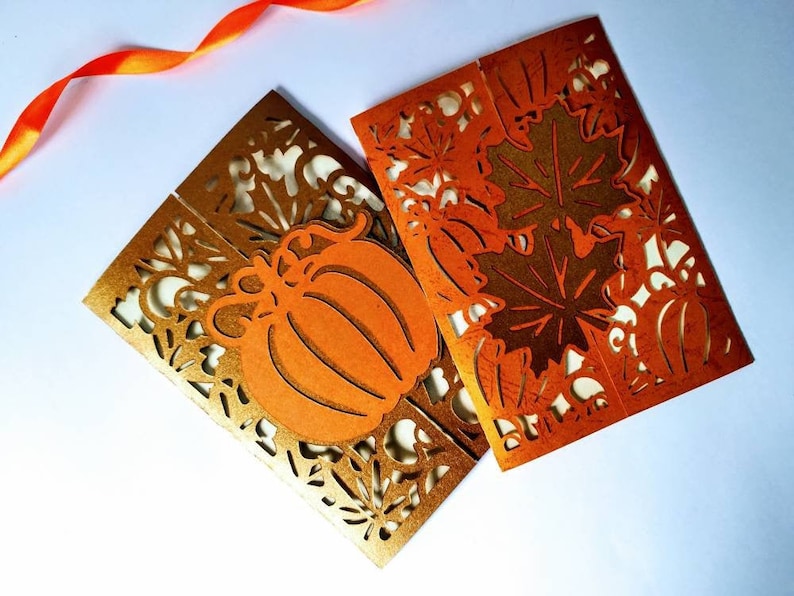 May include: Two folded cards with a fall theme. The cards are orange and gold with a cut-out design of leaves and pumpkins.
