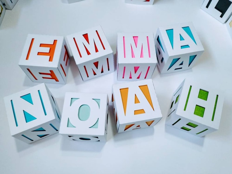 May include: White cardboard boxes with cut-out letters spelling out the name "NOAH" in different colours. The letters are red, orange, yellow, blue, green, and pink.