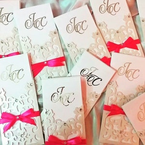 May include: A stack of white cards with a decorative lace pattern and pink ribbon accents. The cards have the letters "JOC" printed in silver on the front.