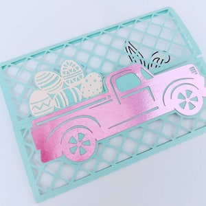 May include: A pink pick-up truck with a white lattice background. The truck is carrying a load of colourful Easter eggs.
