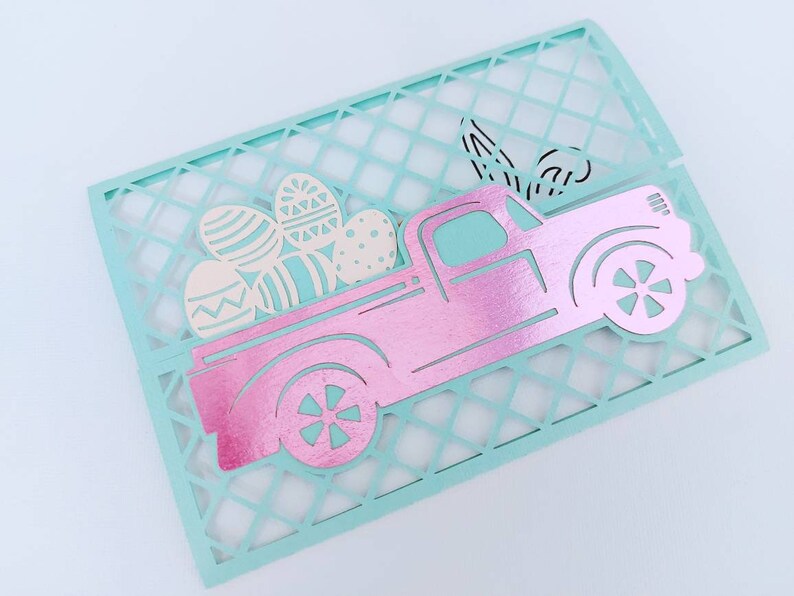 May include: A pink pick-up truck with a white lattice background. The truck is carrying a load of colourful Easter eggs.