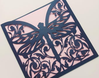 May include: A navy blue laser-cut invitation card featuring a dragonfly design. The dragonfly is centered on a pink background, with intricate floral patterns surrounding it. The card is square-shaped.
