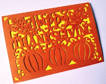 Könnte beinhalten: Orangefarbene Karte mit gelbem Hintergrund und einem ausgeschnittenen Design aus Kürbissen und den Worten "Happy Thanksgiving".