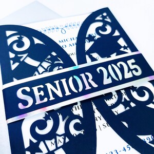 May include: A navy blue graduation invitation with a laser cut design featuring stars and a graduation cap. The invitation has a white band with iridescent foil and the text "Senior 2025".