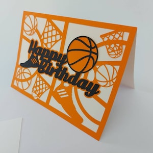May include: Orange card with a white interior. The card is decorated with a black basketball, a black basketball hoop, and the words "Happy Birthday" in black.