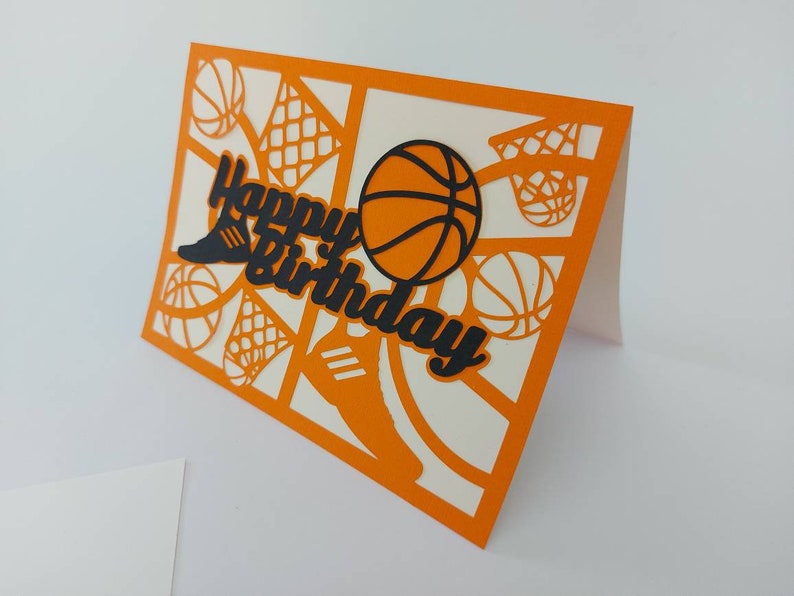 May include: Orange card with a white interior. The card is decorated with a black basketball, a black basketball hoop, and the words "Happy Birthday" in black.