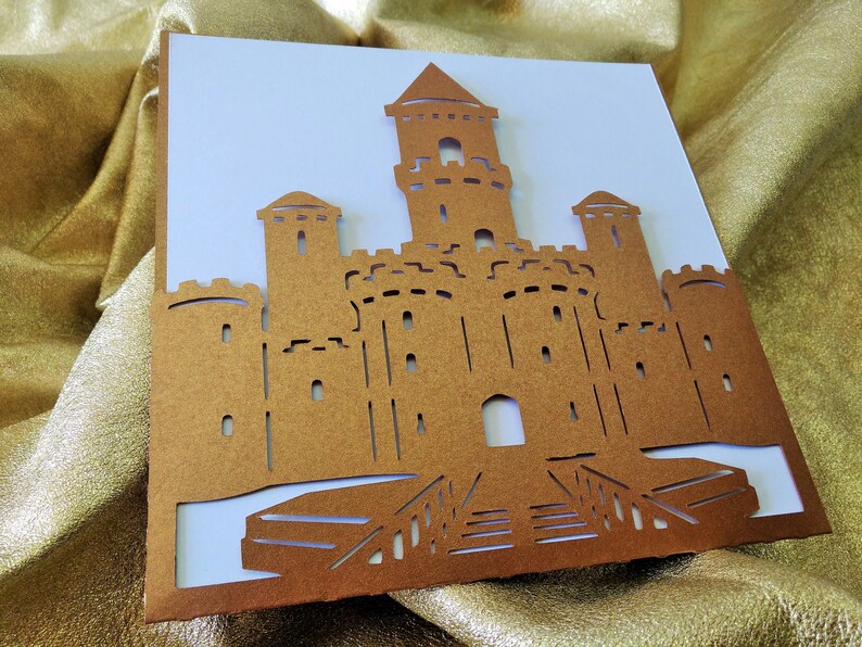 May include: A brown paper castle cutout with a white background. The castle has a tall central tower with two smaller towers on either side. The castle has a gate and a drawbridge.