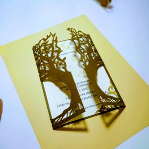 May include: A gold-colored wedding invitation with a laser-cut tree design. The invitation includes the text "Invite We" and event details. The invitation is on a gold background.
