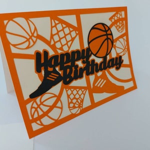 May include: Orange card with a white background and a black cut-out design of basketballs, a basketball hoop, and a shoe. The text "Happy Birthday" is cut out in black.