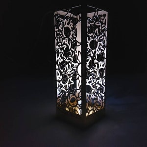 May include: A white, decorative lamp with a geometric design. The lamp is made of a translucent material and has a light inside, casting a warm glow.