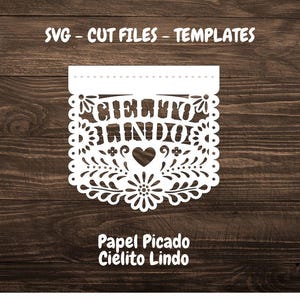 May include: White paper cut-out banner with a floral design and the text "Cielito Lindo" in Spanish. The banner is on a brown wooden background. The text "Papel Picado Cielito Lindo" is below the banner.