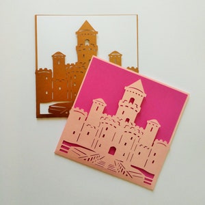 May include: Two paper cards with a castle design cut out. The top card is gold and the bottom card is pink.