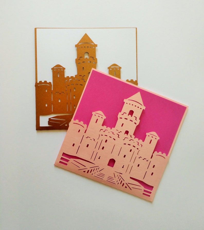 May include: Two paper cards with a castle design cut out. The top card is gold and the bottom card is pink.