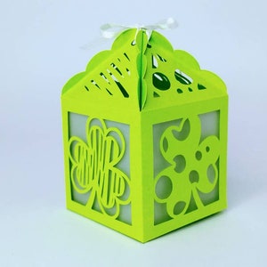 May include: A green paper gift box with a white ribbon. The box has a cut-out design of four-leaf clovers on each side.