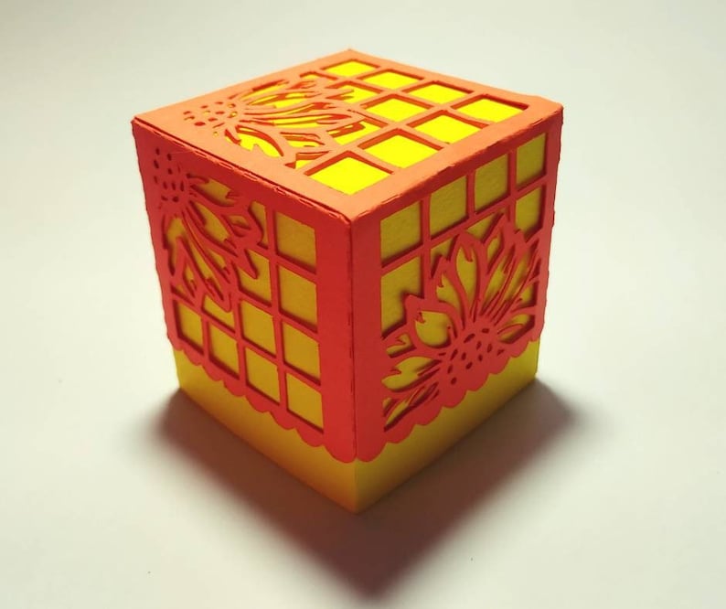 Puede incluir: Una peque&ntilde;a caja cuadrada con una base amarilla y un dise&ntilde;o de corte naranja. El dise&ntilde;o presenta un patr&oacute;n floral y una cuadr&iacute;cula.