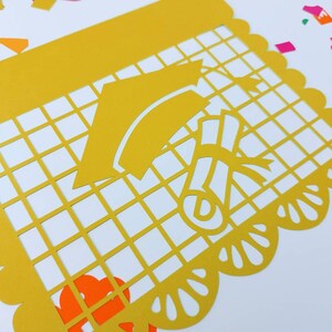 Op de afbeelding: Gele papieren uitsnijding met een ontwerp van een graduatiecap en een diploma. De uitsnijding heeft een gegolfde rand en een rasterpatroon.