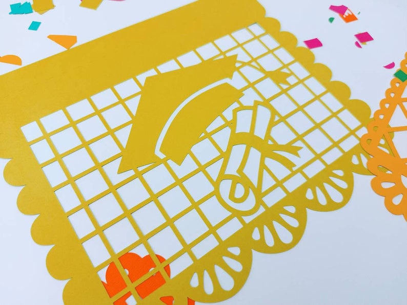 Op de afbeelding: Gele papieren uitsnijding met een ontwerp van een graduatiecap en een diploma. De uitsnijding heeft een gegolfde rand en een rasterpatroon.