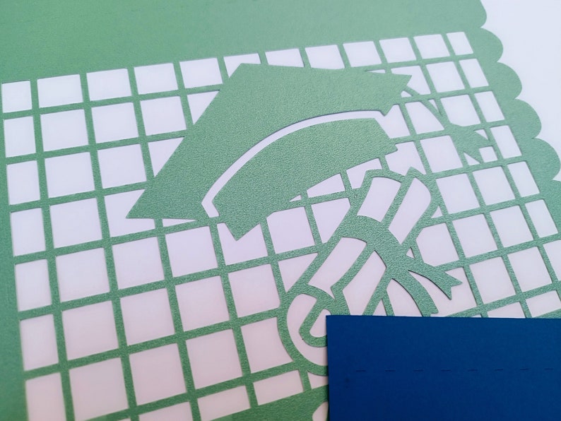 Op de afbeelding: Een groene papieren sjabloon met een ontwerp van een graduatiecap en een diploma. De sjabloon bevindt zich op een witte rasterachtergrond.