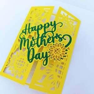 Op de afbeelding: Een gele kaart met een groene "Happy Mother's Day"-boodschap en een zonnebloemontwerp.
