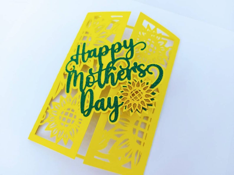 Op de afbeelding: Een gele kaart met een groene "Happy Mother's Day"-boodschap en een zonnebloemontwerp.