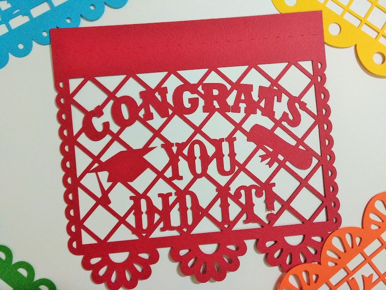 Op de afbeelding: Rode papieren banner met een wit uitgesneden ontwerp met de tekst "Congrats You Did It!" De banner heeft een gegolfde rand en een decoratief patroon.