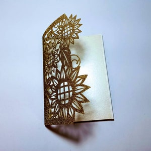 May include: Gold glitter laser cut card with a sunflower design. The card is folded in half and the design is on the front.