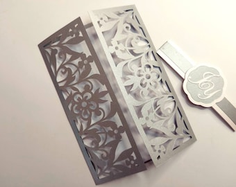 May include: Silver laser cut wedding invitation with a floral design. The invitation is folded in half and has a matching envelope with a silver monogram.