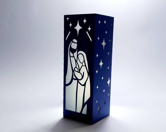May include: A blue paper lantern with a white silhouette of the Holy Family inside. The lantern is decorated with white stars.