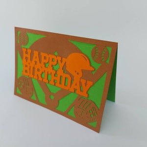 May include: A green and brown card with a baseball theme. The card has a baseball mitt, baseballs, and a baseball helmet cut out of the card. The card says "Happy Birthday" in orange letters.
