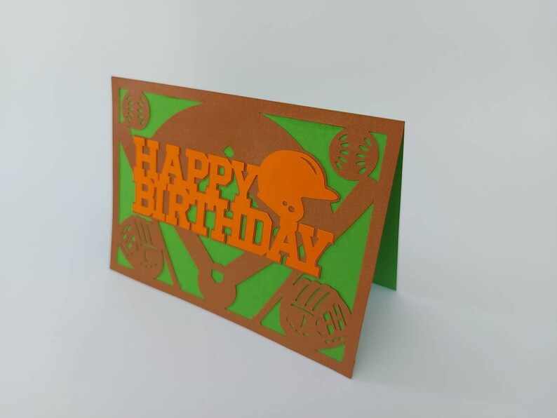 May include: A green and brown card with a baseball theme. The card has a baseball mitt, baseballs, and a baseball helmet cut out of the card. The card says "Happy Birthday" in orange letters.