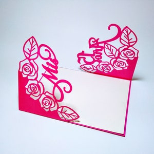 May include: A pink paper card with a cut-out design of roses and leaves. The card is folded in half and the front reads "Mrs."