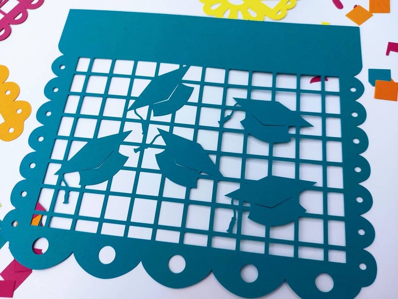 Op de afbeelding: Turquoise blauwe papieren banner met een gegolfde rand en een rasterpatroon. De banner heeft vijf uitgesneden afstudeerhoeden.